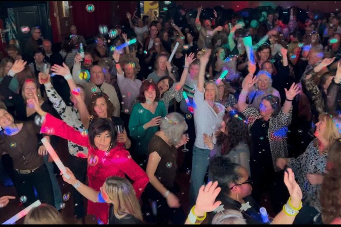 A crowded dance floor with happy dressed up people waving glow sticks