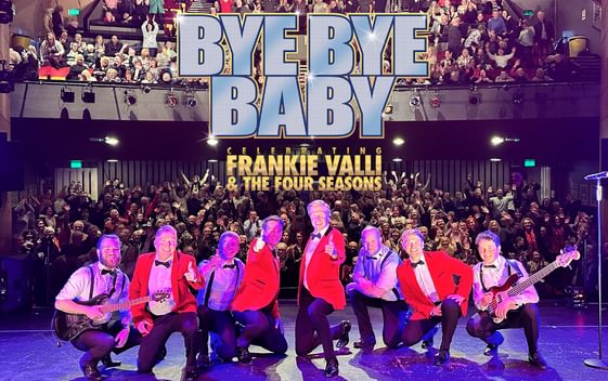 8 cast members crouching down on stage with audience behind them cheering. Bye Bye Baby written in silver Frankie Valli & the Four Seasons written in gold.