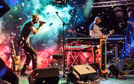 Colourful confetti falling with white stage mist surrounding a man singing and man playing guitar.