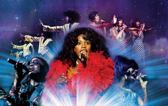 The cast of Magic of Motown are seen in costume and singing into microphones, arranged in two arcs on a purple and blue sparkling background