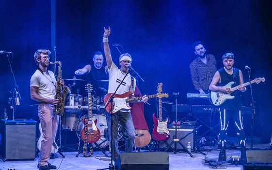 The cast of "Money for Nothing" are shown on stage, playing their instruments and dressed as the members of Dire Straits
