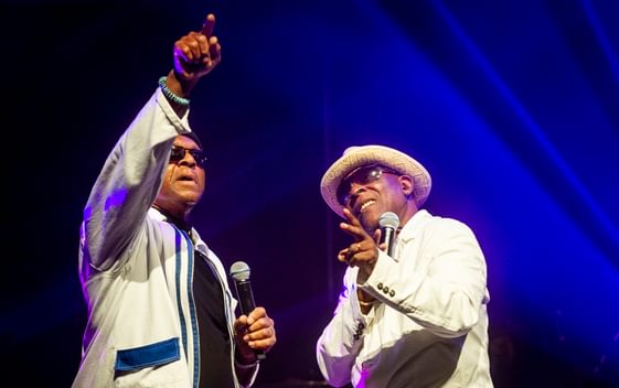Two singers from the band The Real Thing both dressed in white holding microphones