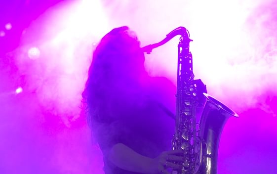 A silhouette of a performer playing the saxophone in pink lighting and haze