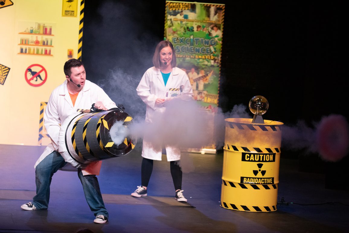 A man in a white jacket holding a metal container with smoke a lady in white jacket watching