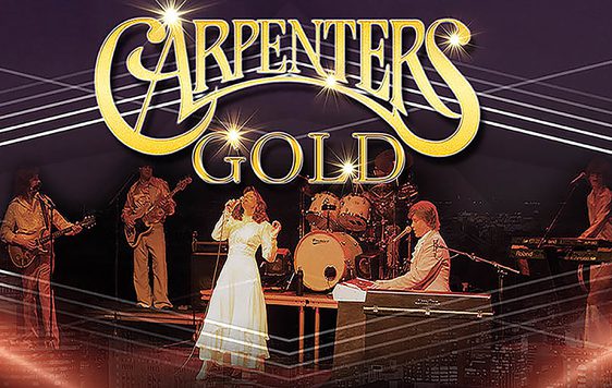 A band performing on stage as "The Carpenters" with light beams surrounding them. The show title "Carpenters Gold" is shown at the top of the image