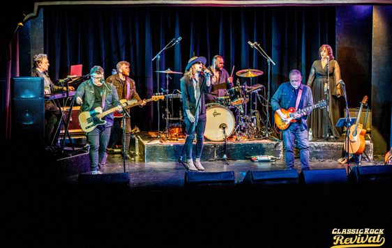 A 7 piece band performing on stage with a black backdrop