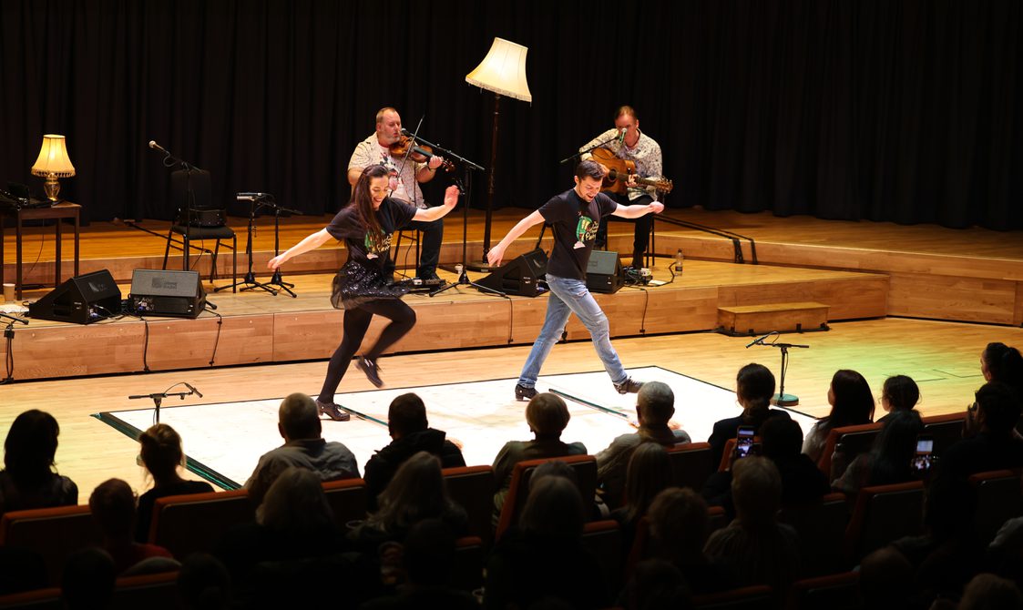 2 members of the Irish House Party band are Irish Dancing on a wooden board on a stage.