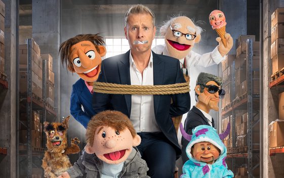 Paul Zerdin is stood in a warehouse tied up with tape over his mouth, surrounded by puppets.