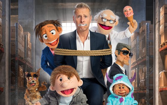 Paul Zerdin is stood in a warehouse tied up with tape over his mouth, surrounded by puppets.