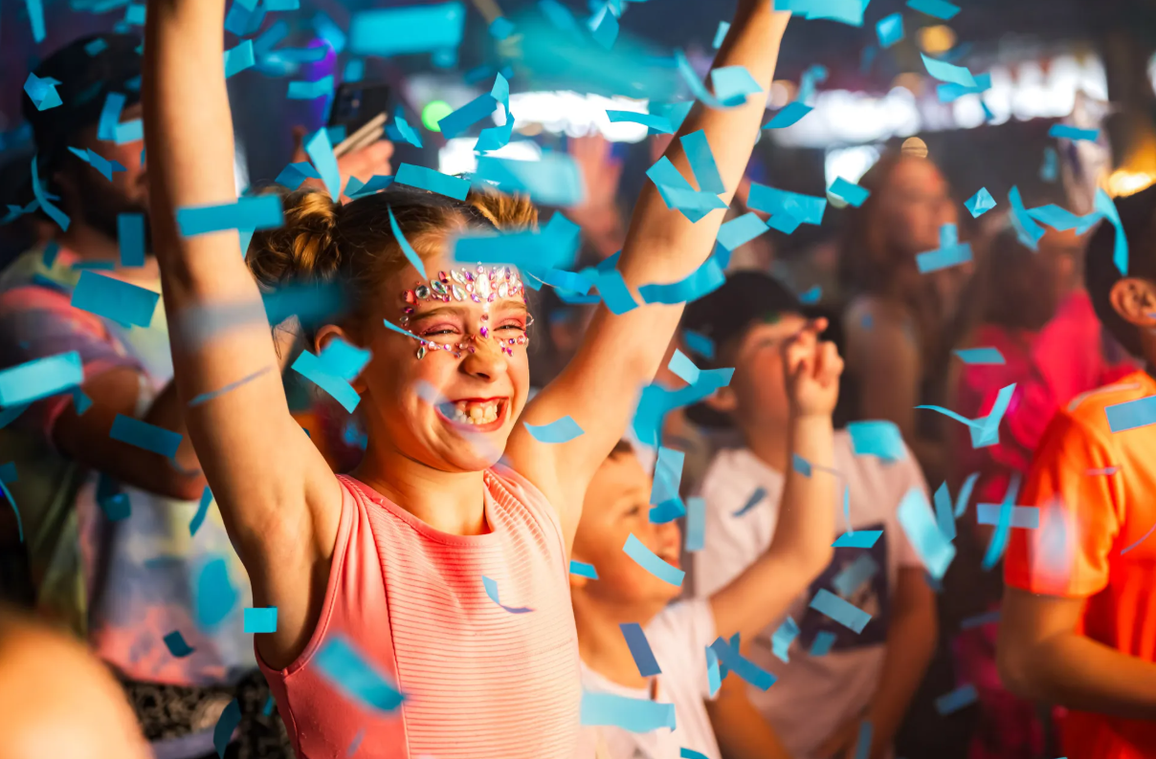 Young girl smiling with arms in the air as blue confetti falls from above.