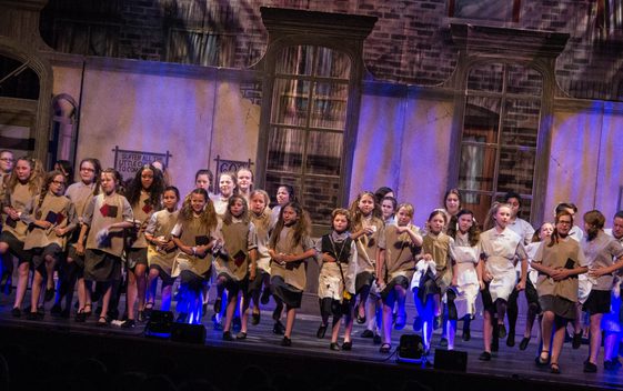 Children performing on stage in raggy clothes in a performance of Annie