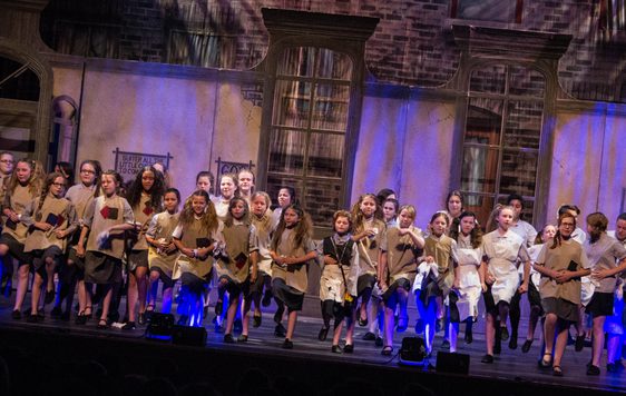 Children performing on stage in raggy clothes in a performance of Annie