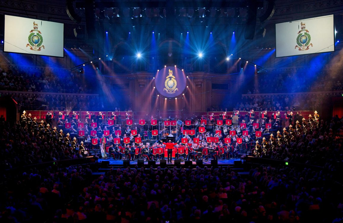 40 royal marines stood in a tiered semi-circle in full military unform lit in blue and white lights.