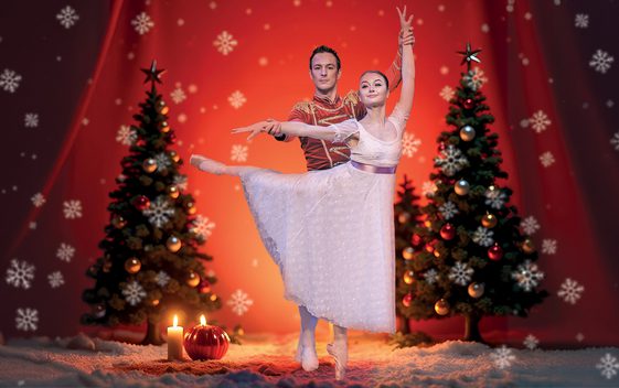 A male and a female ballet dancer are dancing on stage with a backdrop of snow, Christmas trees and candlelight.