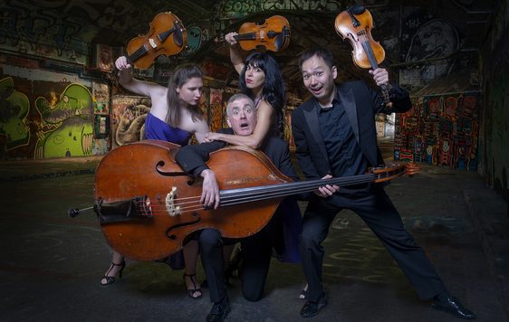 The band members of Graffiti Classics are in a pose which looks like they are fighting with their string instruments in an underpass.