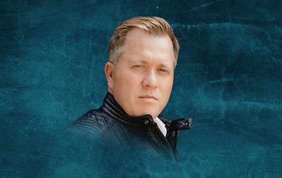 Tony Stockwell, wearing a leather jacket, is shown against a dark blue background