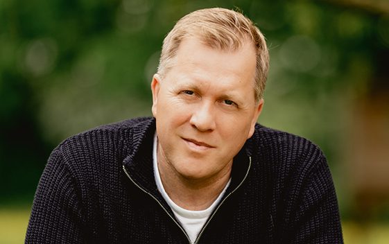 Psychic Medium Tony Stockwell wearing a dark sweatshirt against a blurred green foliage backdrop