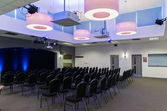 Camberley Theatre Function Room with chairs laid out in rows, facing a small stage area with black curtains and blue uplighters on the stage