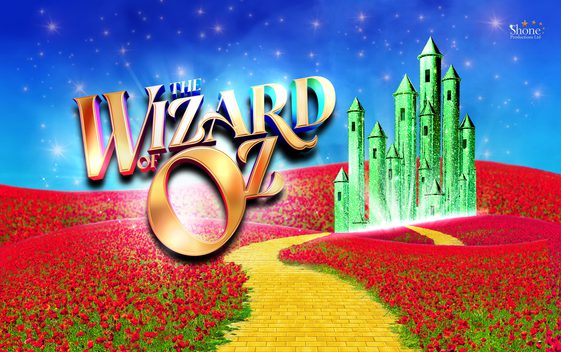 The show title "the Wizard of Oz" written in gold set against a background showing red fields, a yellow brick road and a green castle.