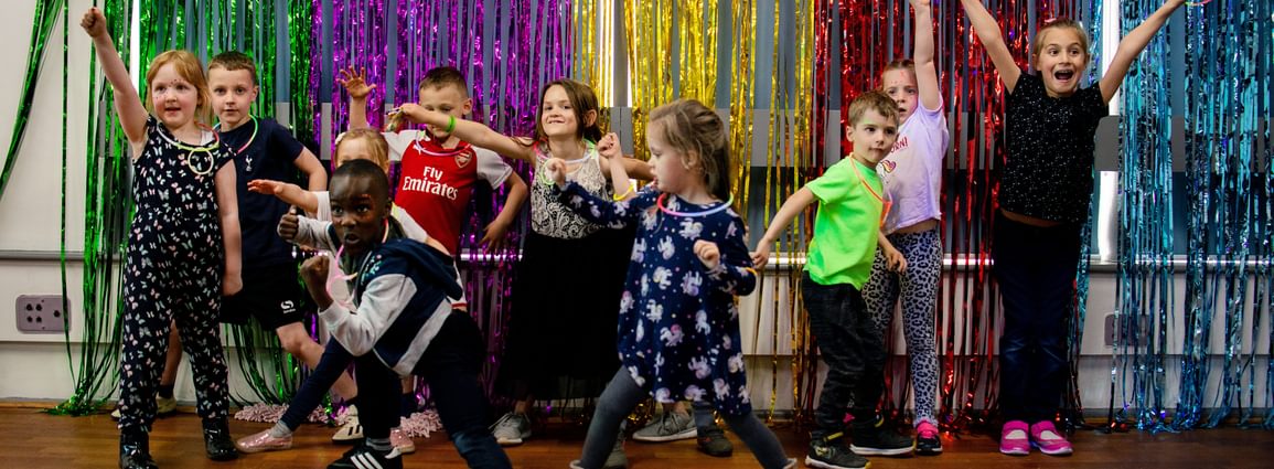 A group of children dance and pose in front of multicoloured foil strip curtains