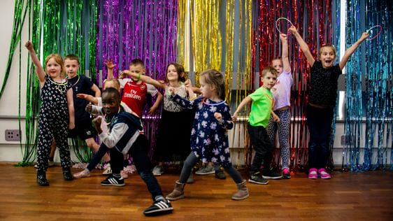 A group of children dance and pose in front of multicoloured foil strip curtains