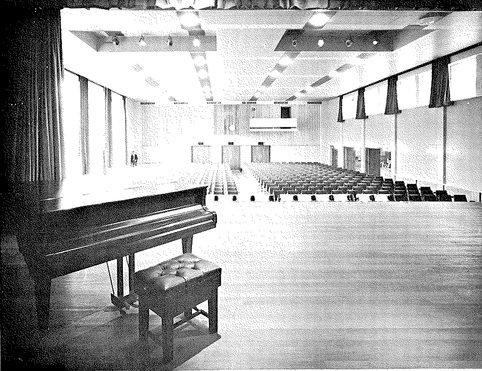 A black and white photo from the Camberley Civic Hall taken from the stage, showing a baby grand piano to the left and stalls seating in the main auditorium.