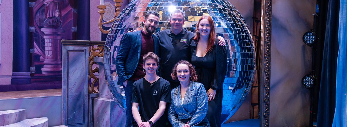 Members of the Camberley Theatre team are posing in front of a giant Mirrorball on stage