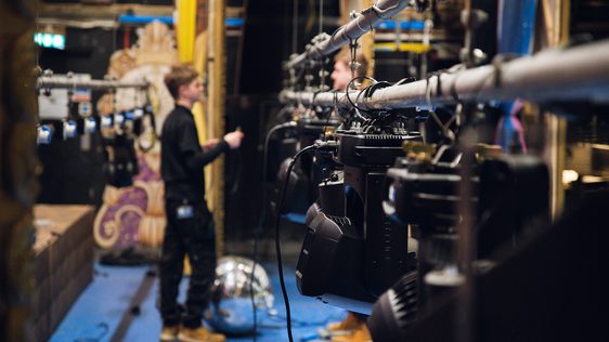 A technician is rigging lights to a bar on stage