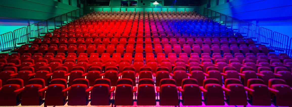 A front facing view of all of the red seats at Camberley Theatre lit up green, red and blue