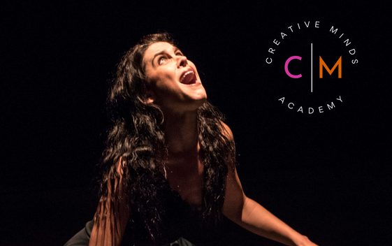 A young performer is lit from above against a black background. They are looking up into the light and shouting