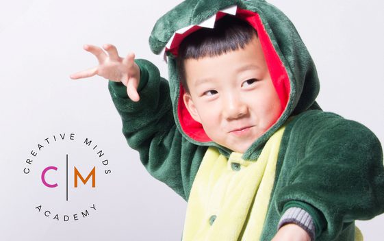 A young child is wearing a dinosaur costume and posing with their hands like claws