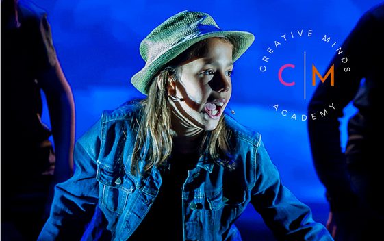 A young performer on stage wearing a hat and a denim jacket and they are singing